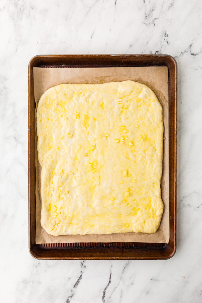 Brushing pizza dough with garlic butter to make cheesy breadsticks.