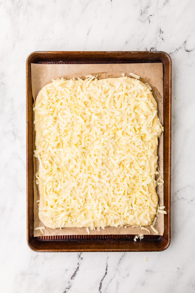 Adding cheese to garlic breadsticks from pizza dough.