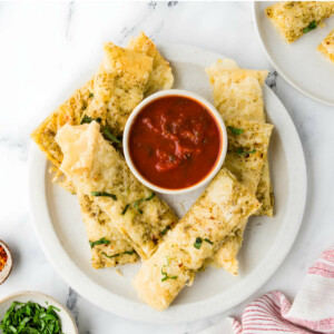 Cheesy breadsticks made from pizza dough on a plate with marinara sauce.