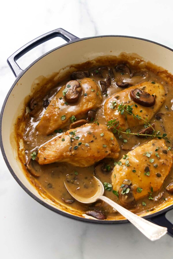 A skillet with four chicken breast in mushroom sauce.