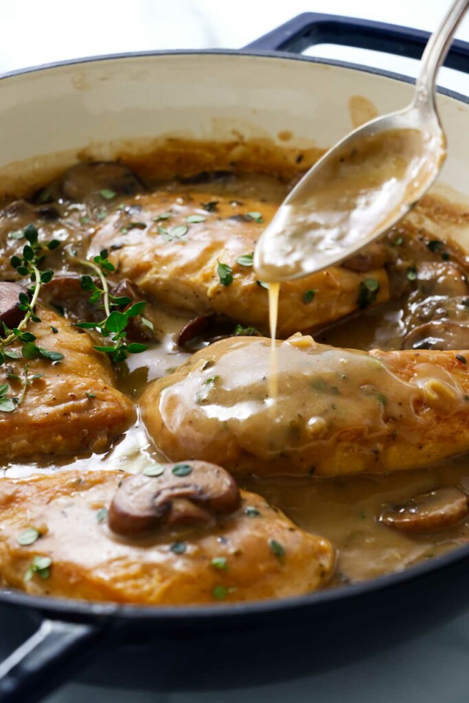 A spoon drizzling sauce over chicken in mushroom sauce.