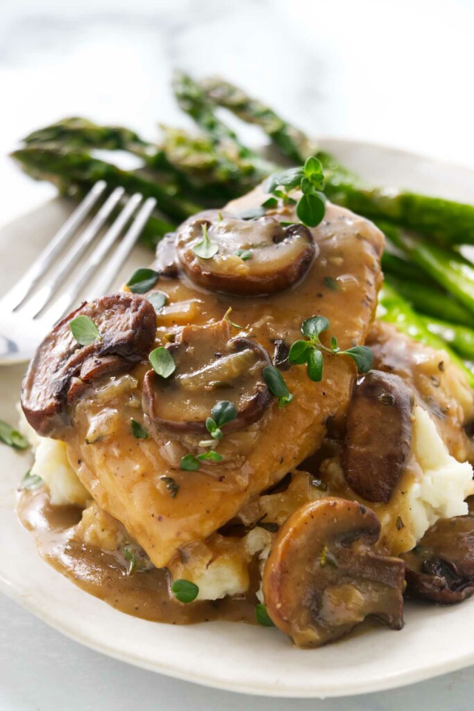 Chicken and mushroom sauce on a plate with mashed potatoes and asparagus.