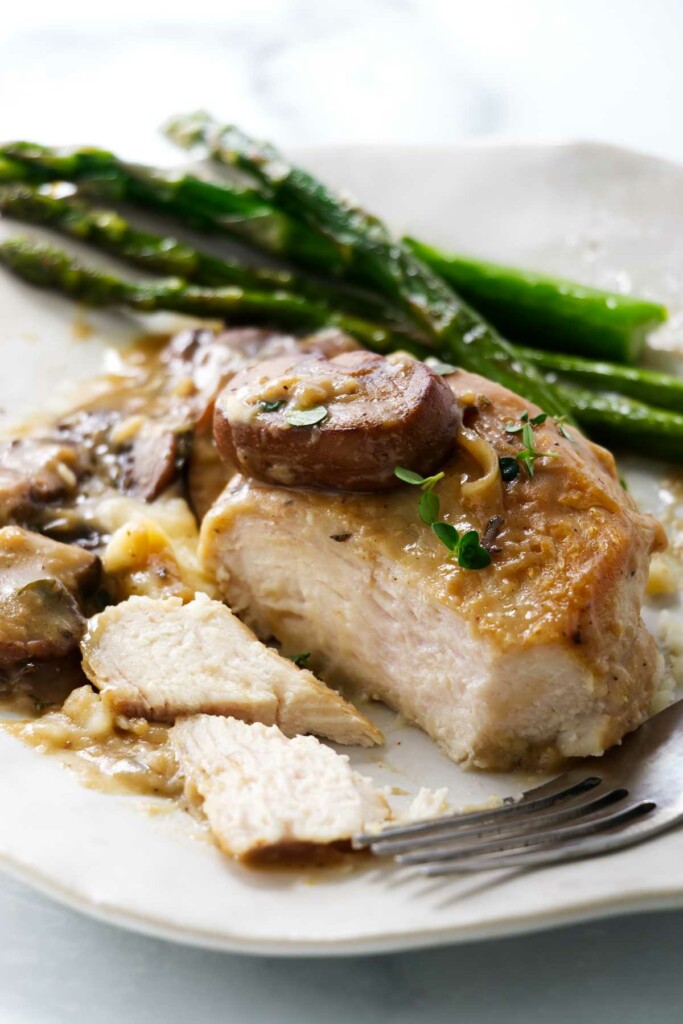 Plate with roasted chicken in mushroom sauce next to sautéed asparagus.