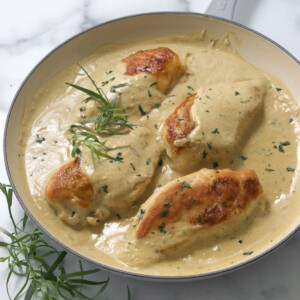 A tarragon chicken recipe in a skillet with fresh tarragon.