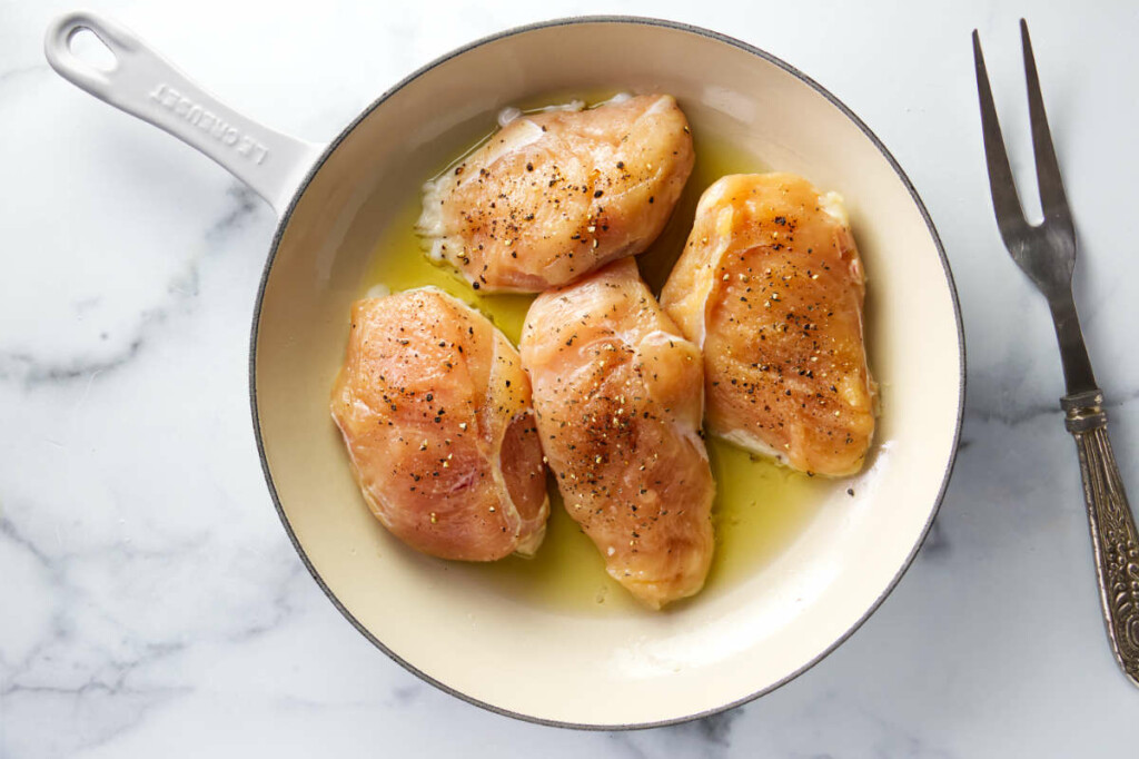 Adding chicken breasts to a skillet with hot oil.