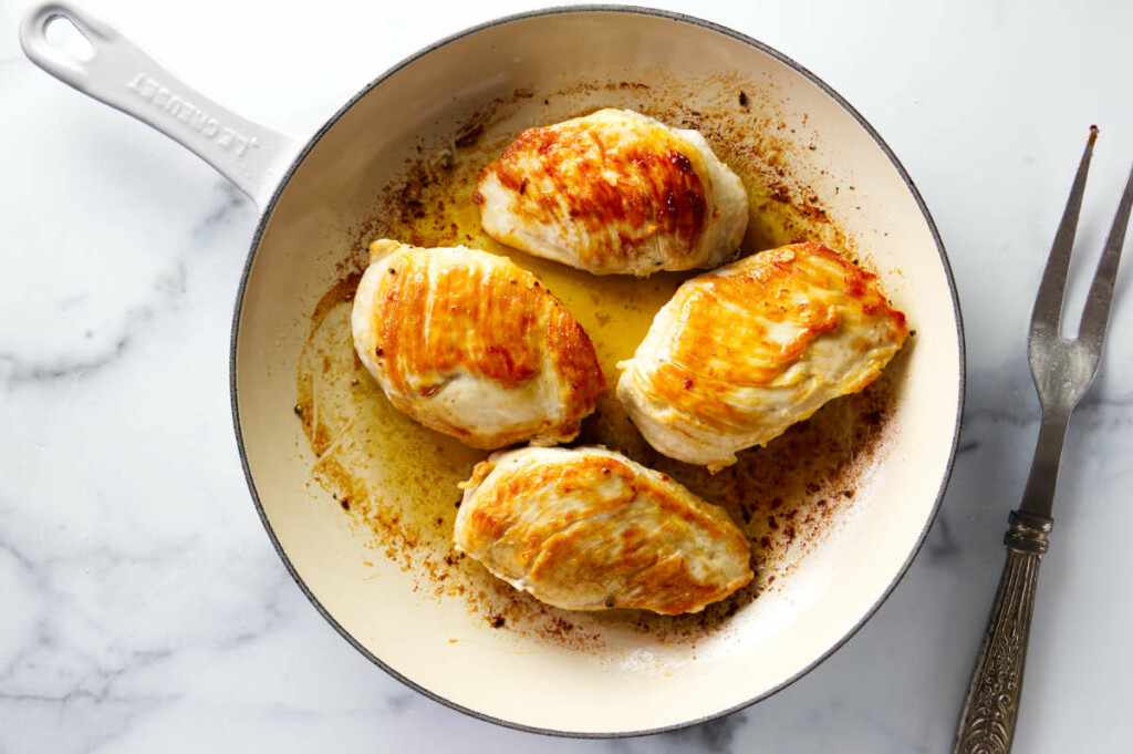 Four seared chicken breast in a skillet for making tarragon chicken in cream.