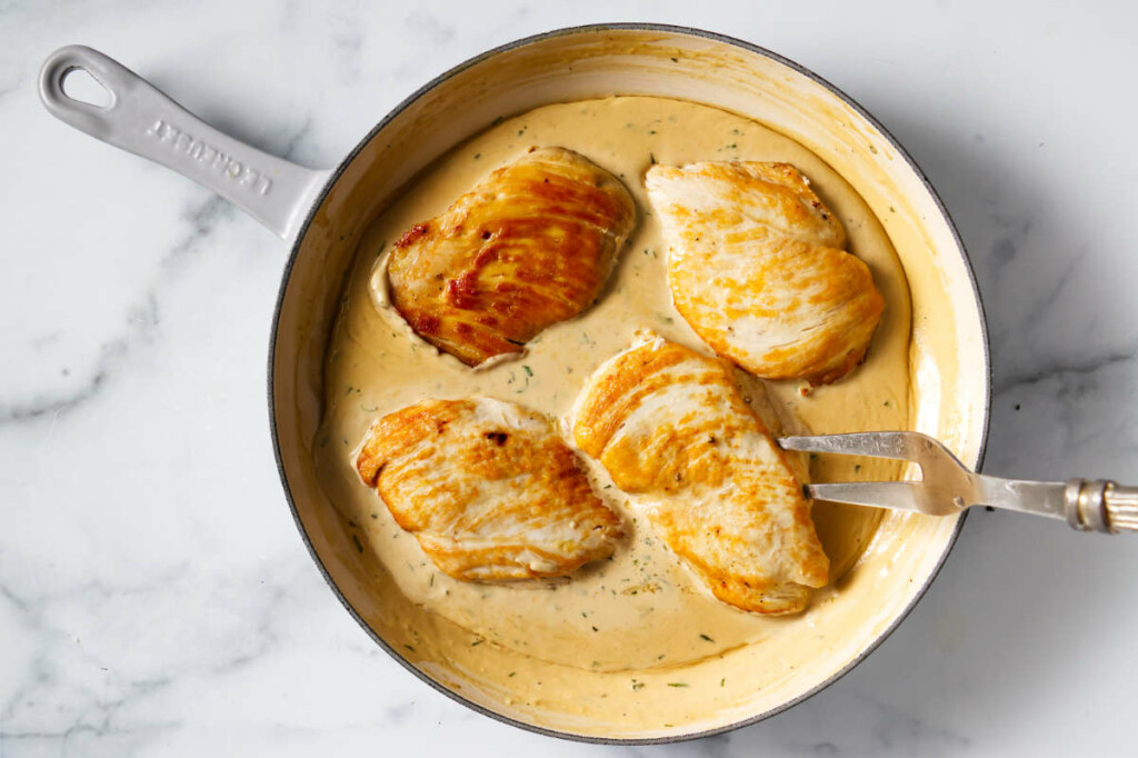 Placing the chicken breasts in creamy tarragon sauce.