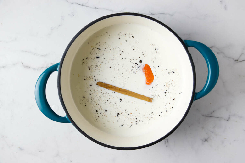 Adding cinnamon and an orange peel to the pot for rice pudding dessert.