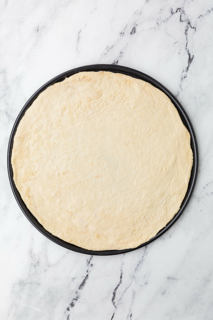 Unbaked pizza dough on round baking pan.