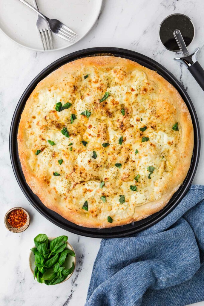 Homemade pizza with cheese and basil on a black tray.