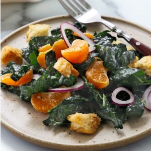 A kale mandarin orange salad on a plate with a fork.