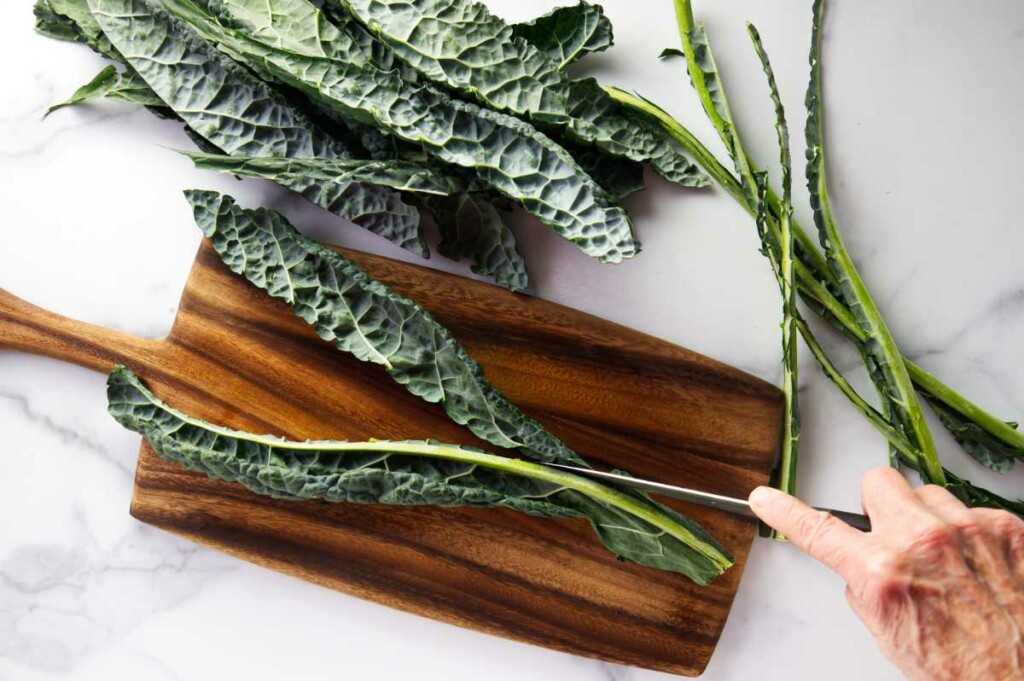 A knife slicing kale leaves off the rib of the kale.