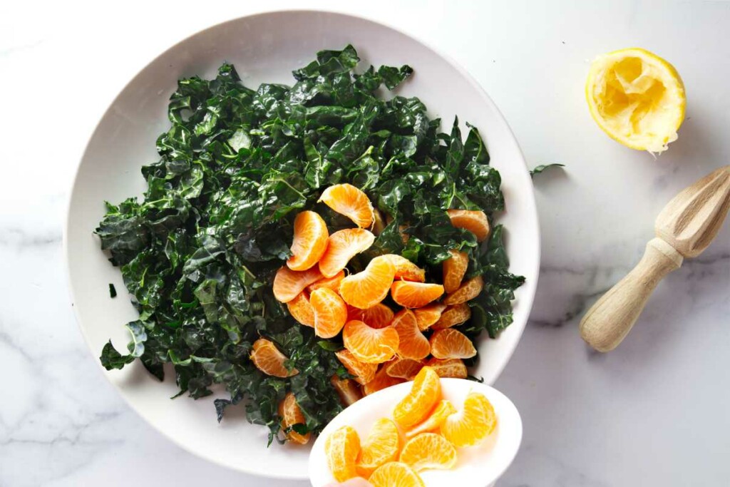 Adding orange slices to a bowl of kale for salad.