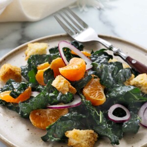 A plate filled with kale and mandarin salad next to a fork.