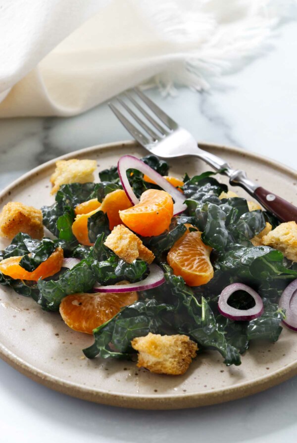 A plate filled with kale and mandarin salad next to a fork.