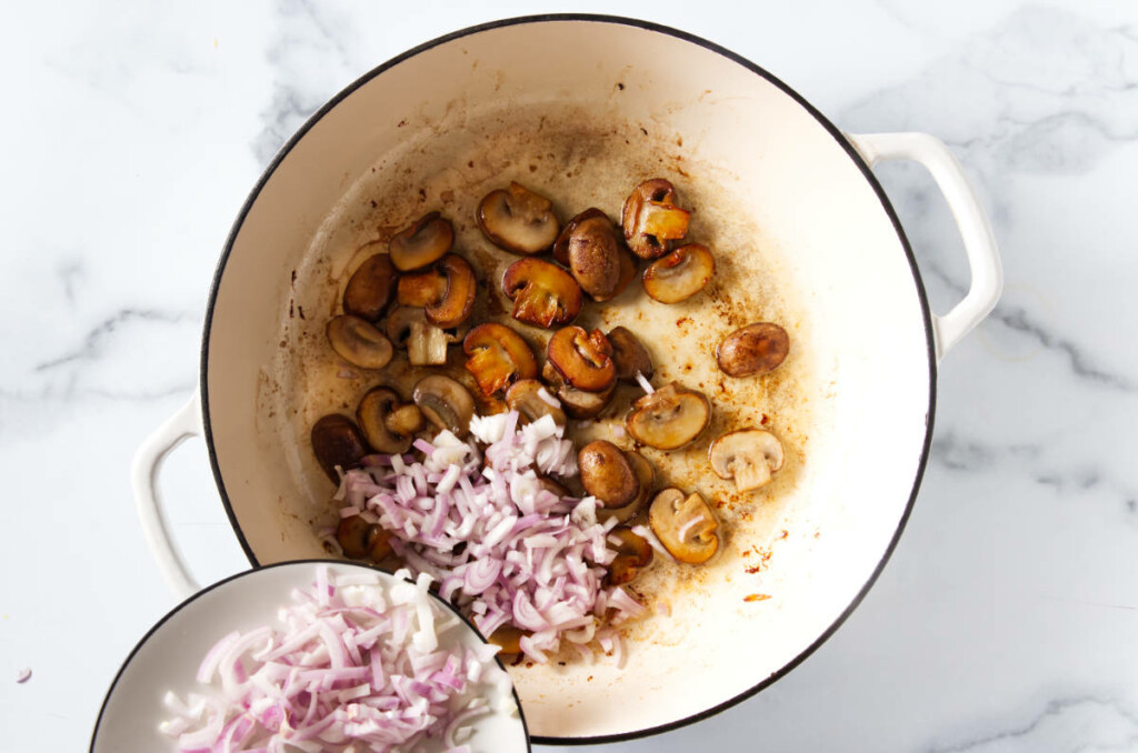 Onions being added to sautéed mushrooms.