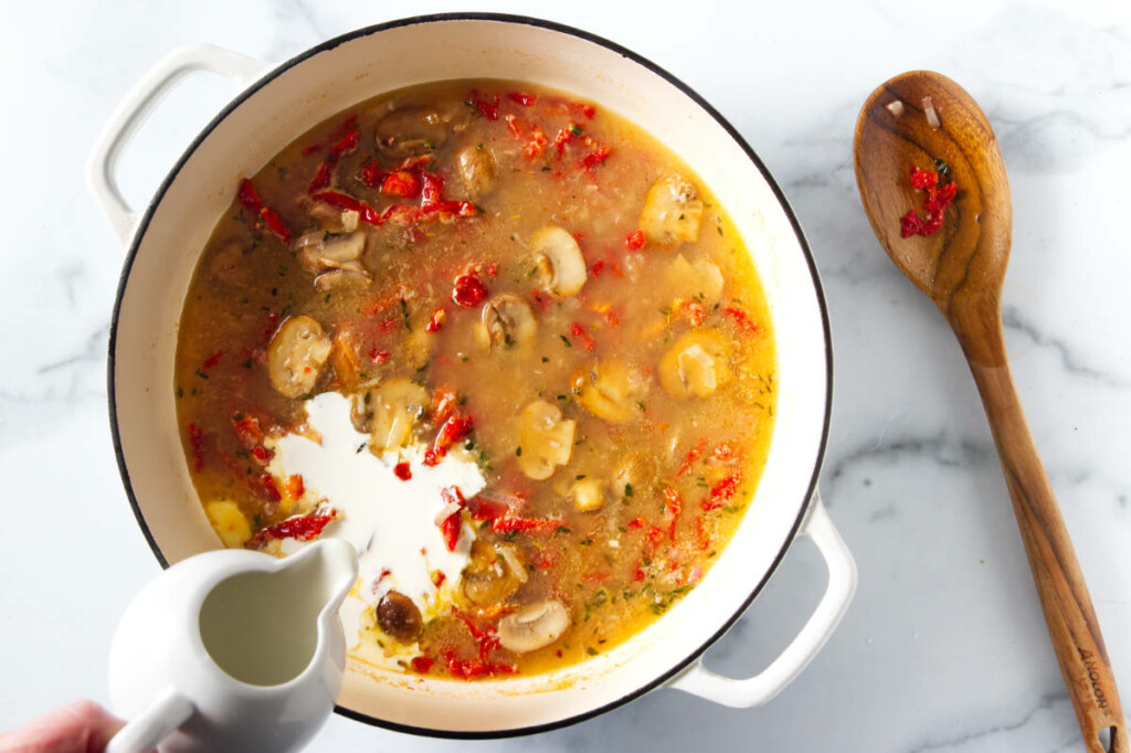 Adding cream to a pot of sauce preparation, wooden spoon alongside the pot.