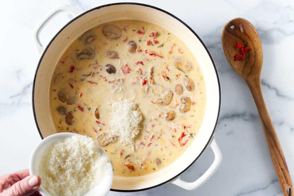 Adding cheese to a pot of creamy lemon pasta sauce. A wooden spoon alongside the pot.