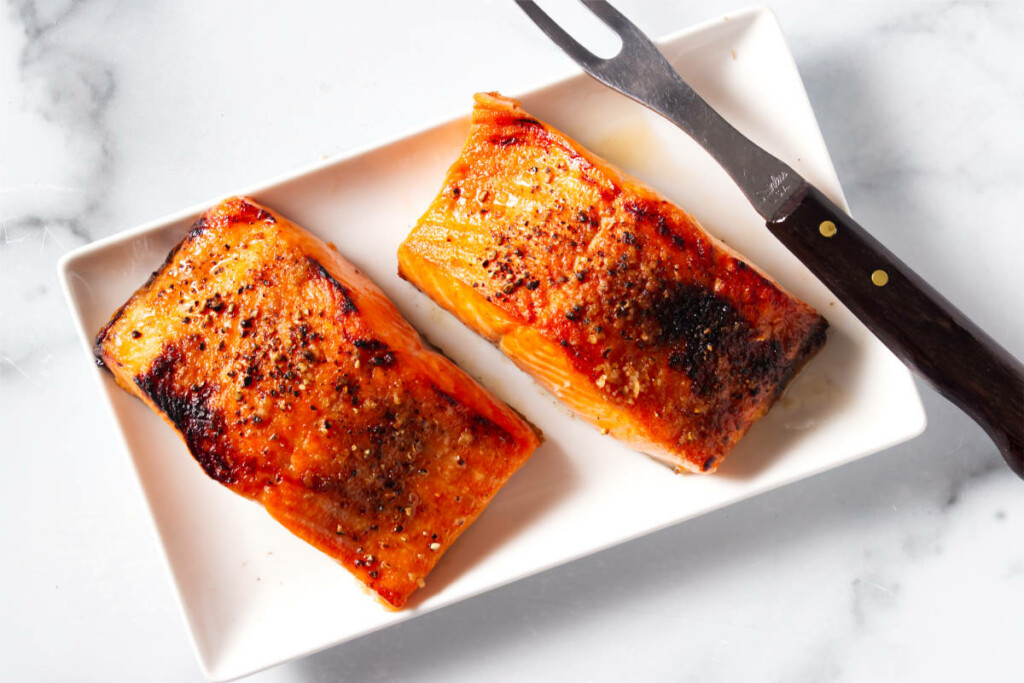 Two servings of broiled salmon on a plate with a serving fork.