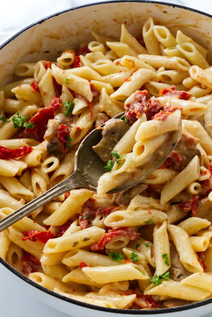 A serving spoon in a pot of penne pasta.