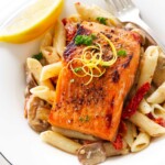 A serving of broiled salmon in a dish of pasta with mushrooms, sun-dried tomatoes and lemon cream.sauce.