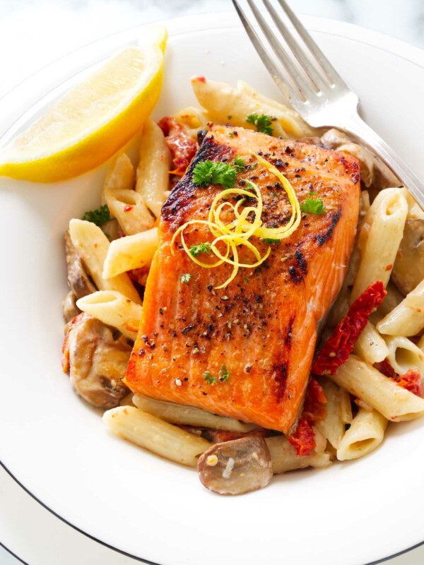 A serving of broiled salmon in a dish of pasta with mushrooms, sun-dried tomatoes and lemon cream.sauce.