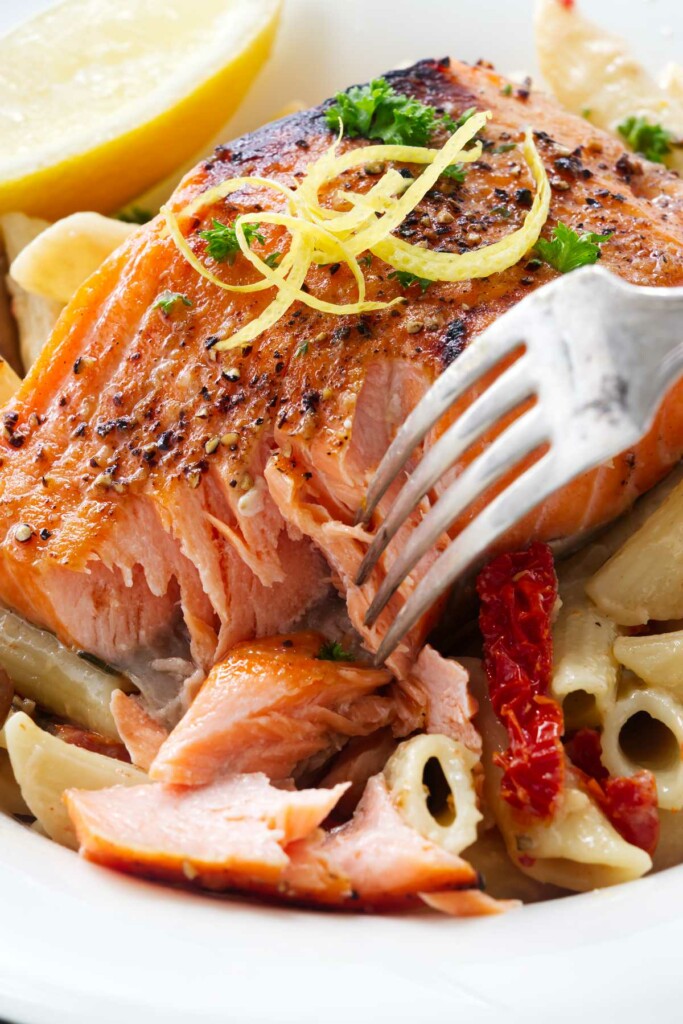 Close up of a serving of pasta and salmon with a dinner fork taking a bite of salmon.