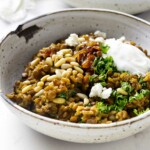 A bowl filled with lentils and rice with caramelized onions and a dollop of yogurt.