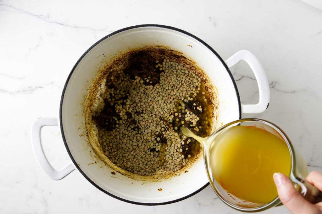 Adding lentils and chicken broth to the pot.