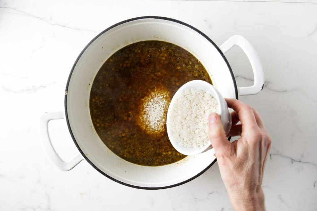 Adding white rice to the lentils in a large pot.