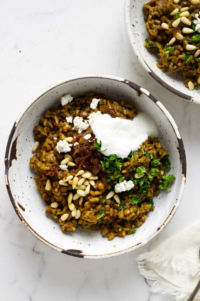 Two bowls of mujadara rice and lentils topped with onions.