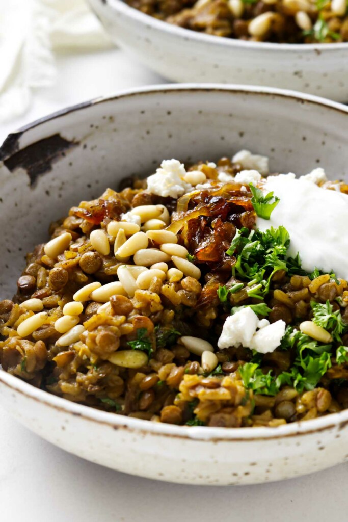 A bowl of lentils and rice topped with caramelized onions, feta, and yogurt.