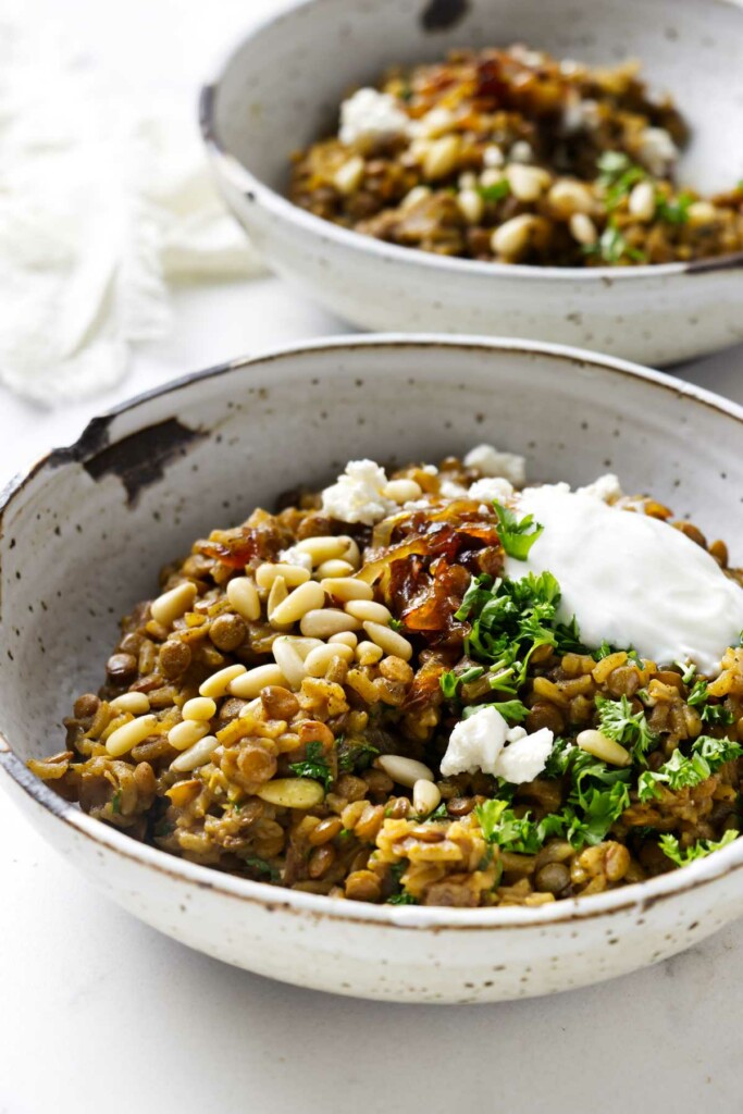 Lentil rice and onions in two bowls topped with parsley, yogurt, and feta.