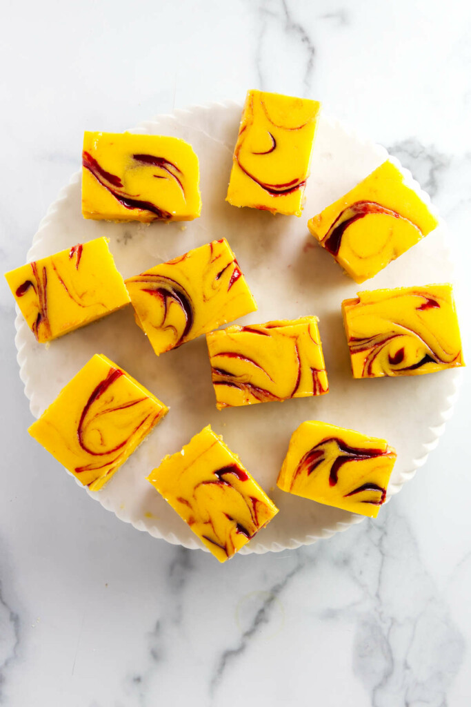 Top view of nine square mango swirl cheesecake bars on a round, white plate.