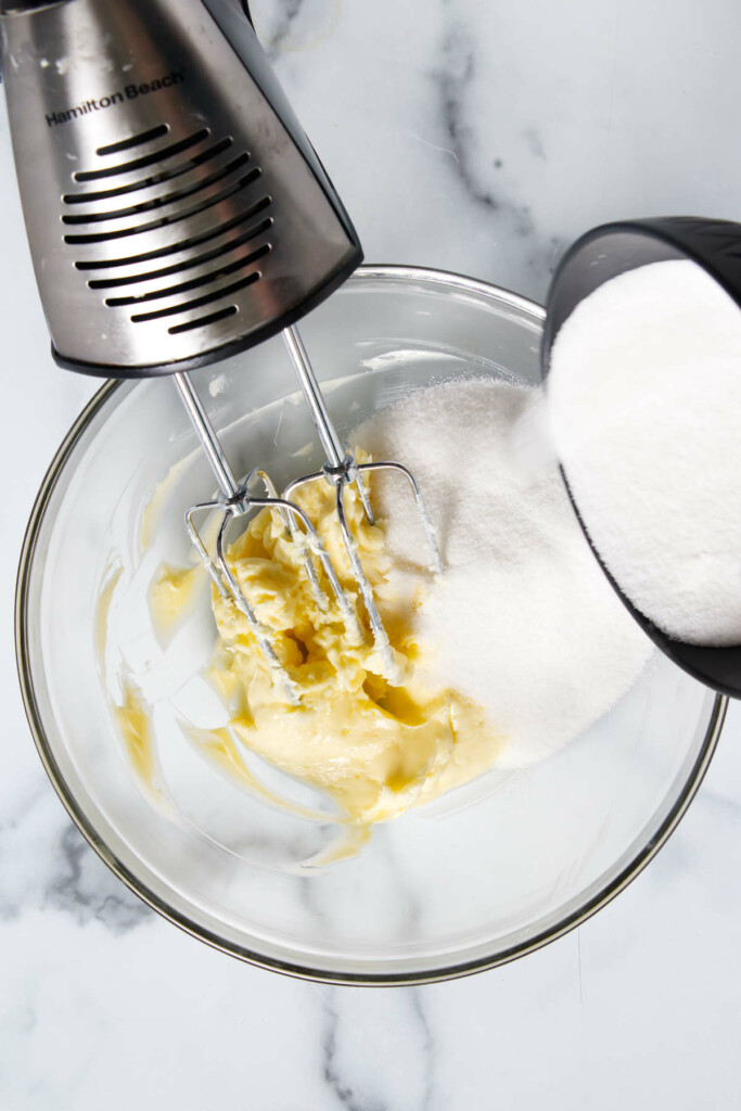 An electric mixer is positioned over a glass bowl containing softened butter.