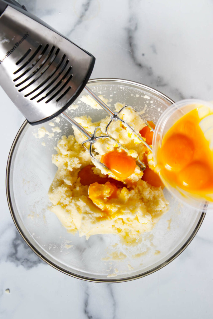 A hand mixer is in a glass bowl with butter and sugar, preparing the base for mango dessert bars.