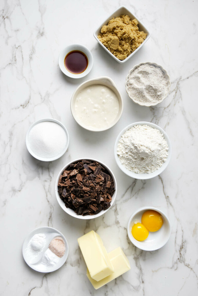 Baking ingredients on marble: brown sugar, vanilla, buttermilk, flour, chocolate chunks, eggs, baking soda, salt, sourdough starter discard.