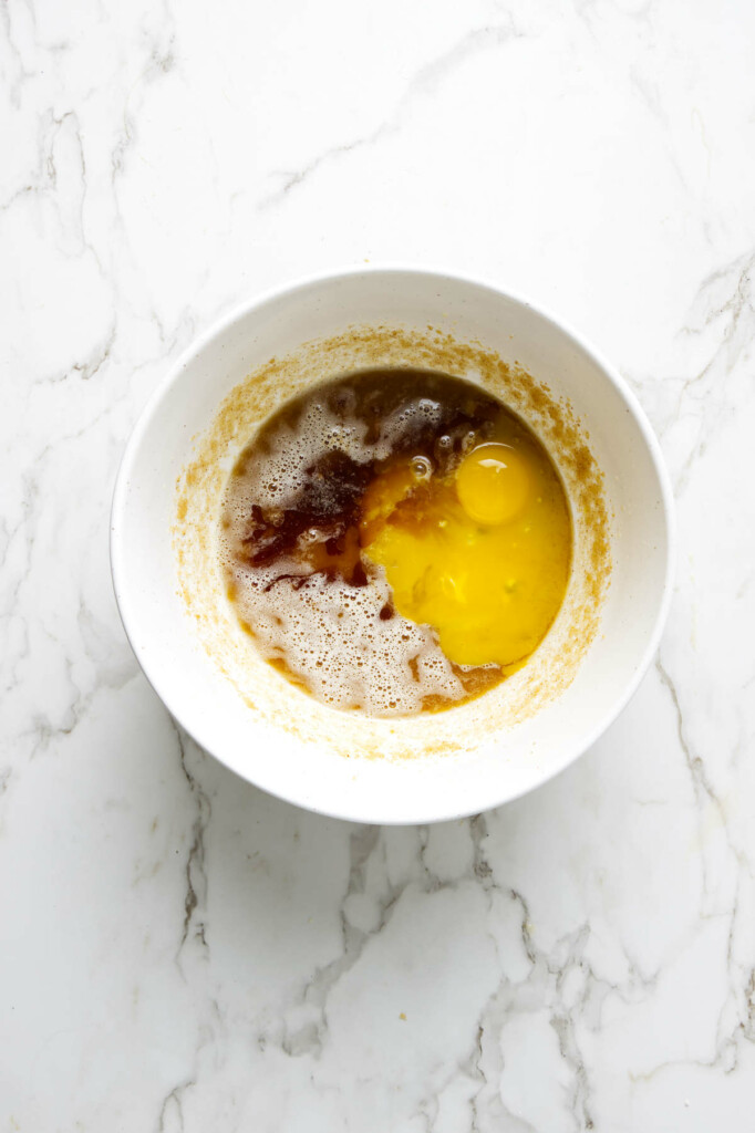 A white bowl with butter, egg, and vanilla extract partially making sourdough chocolate chip cookies.