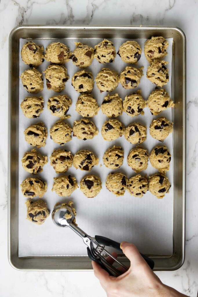 Scooping sourdough chocolate chip cookie dough onto a parchment-lined baking sheet.