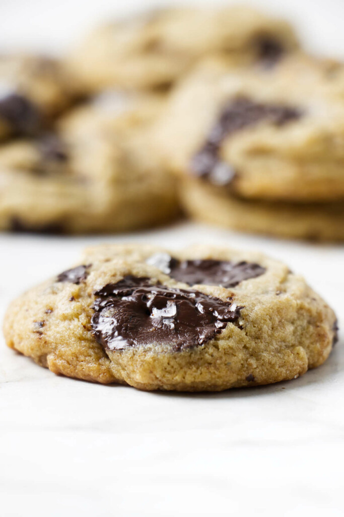 A gooey sourdough discard chocolate chip cookie with melty chunks; blurred cookies in the background.