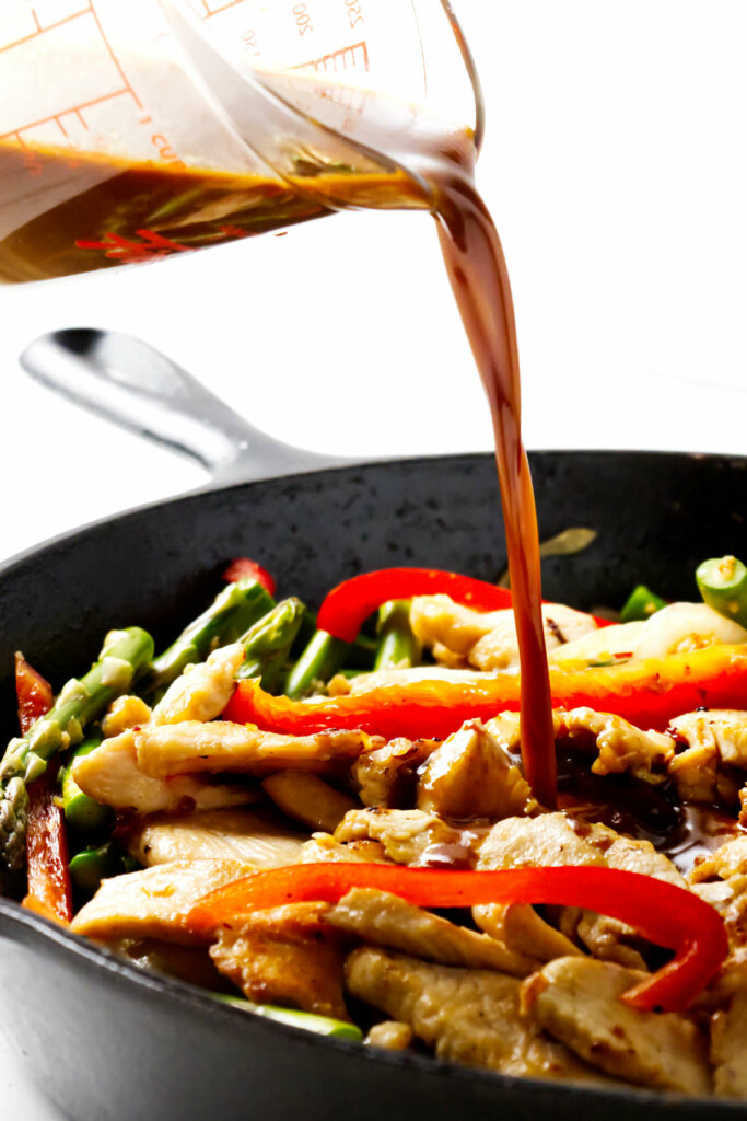 Pouring a homemade quick stir fry sauce into a wok with chicken stir fry.