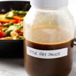 A homemade stir fry sauce recipe in a large jar next to a chicken stir fry.