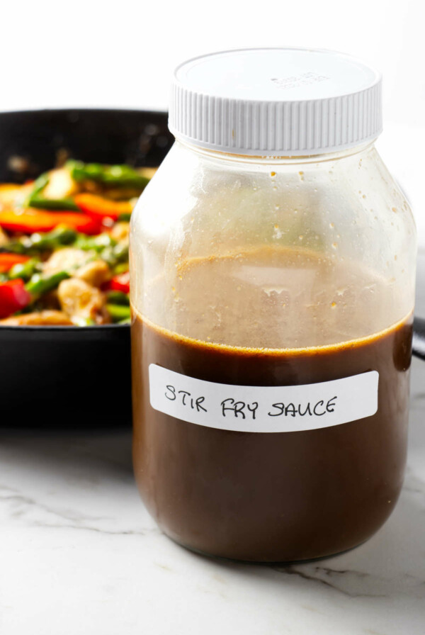 A quick Asian stir fry sauce mixed in a large jar sitting in front of a chicken stir fry.