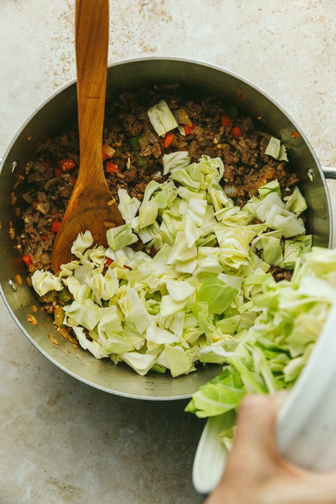 Adding chopped cabbage to a soup pot.