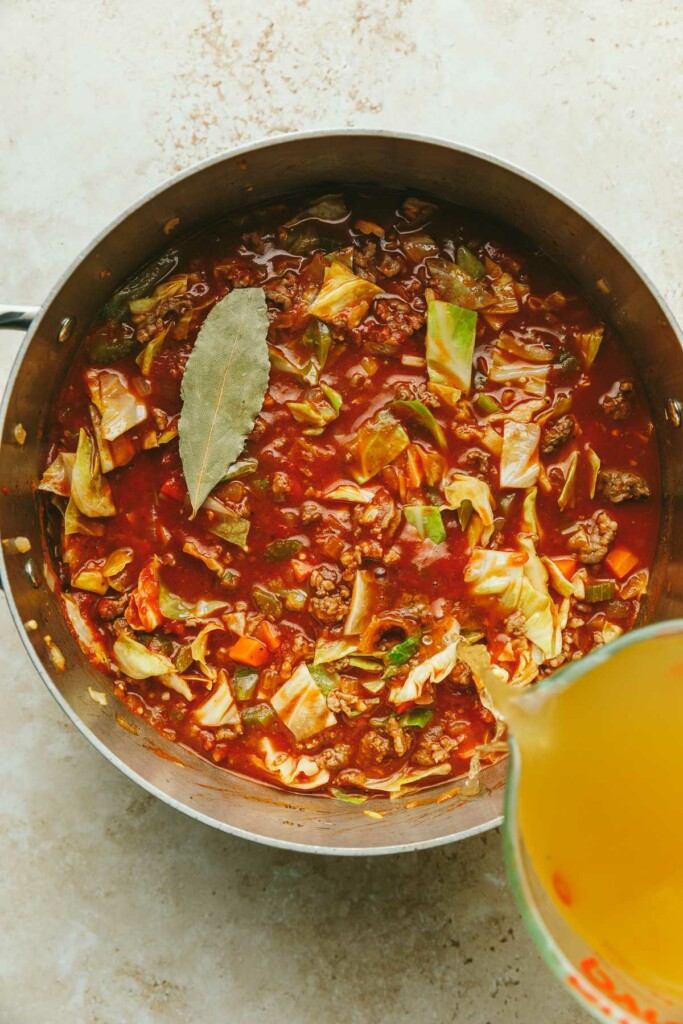 Adding broth to a pot of stuffed cabbage rolls soup.