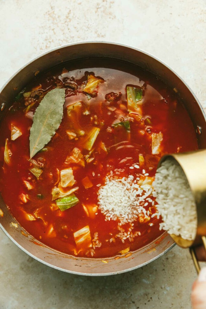 Adding rice to a pot of stuffed cabbage roll soup.