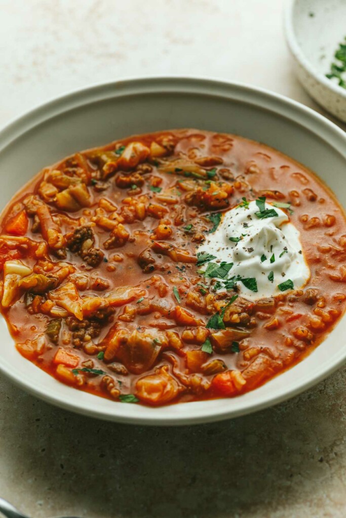 A bowl of stuffed cabbage soup with a dollop of sour cream.