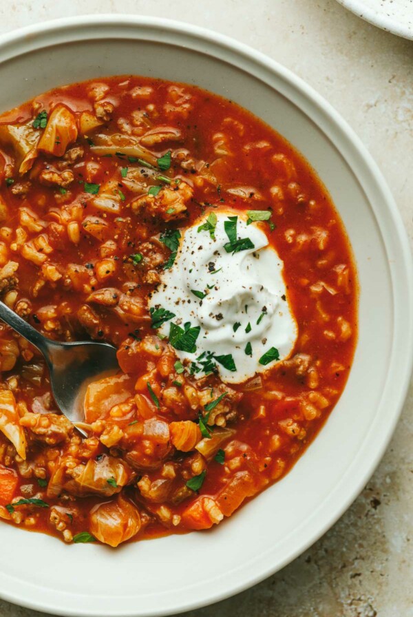 A bowl of unstuffed cabbage roll soup with sour cream and a spoon.