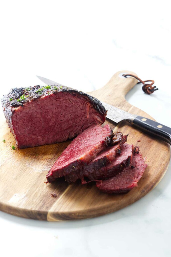 Baked corned beef on a cutting board with a knife.