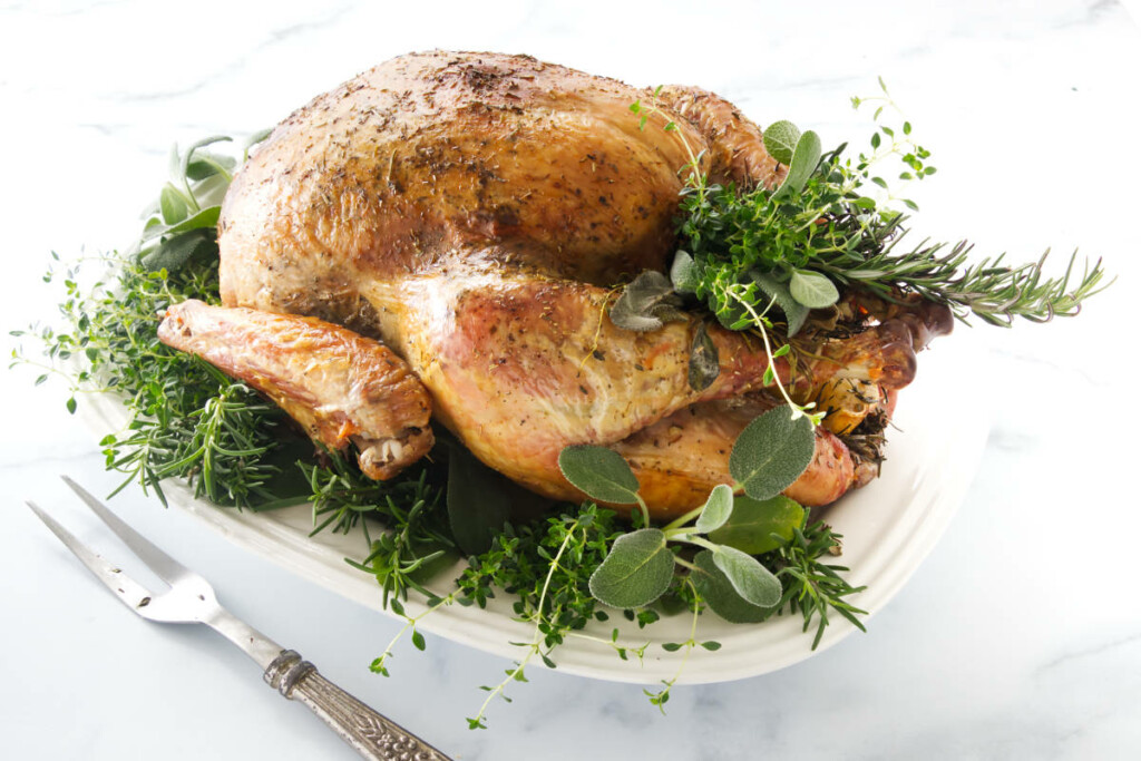 Herbs surrounding a golden brown roasted turkey.